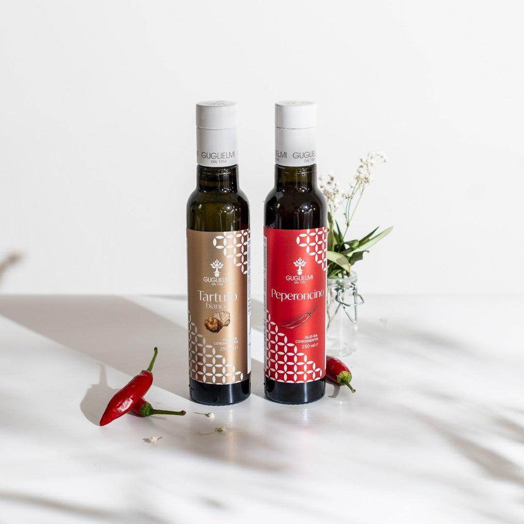 Guglielmi flavored olive oil set featuring truffle and chili bottles with red peppers and floral decoration on white surface