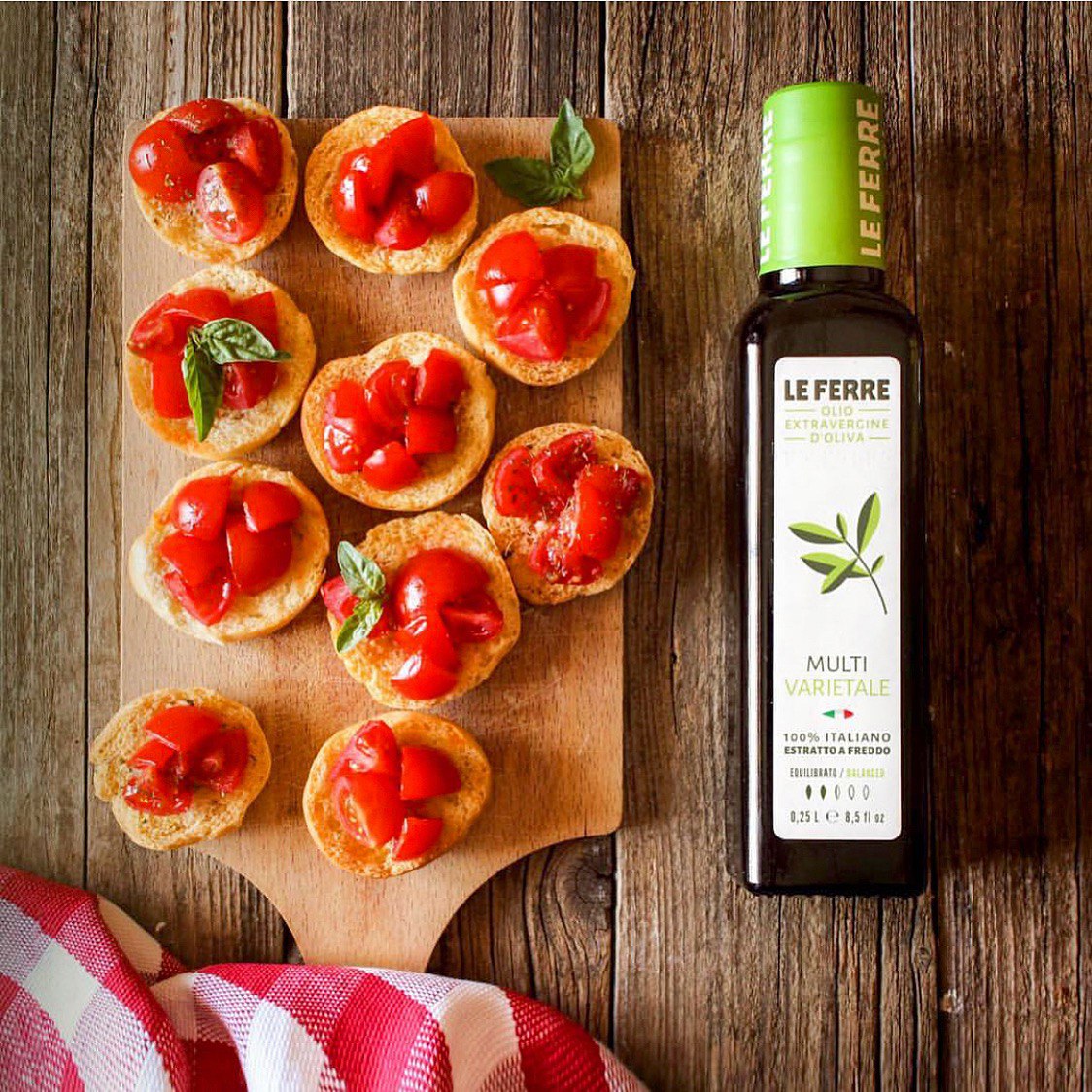 LeFerre Multivarietale olive oil bottle next to bruschetta topped with fresh tomatoes and basil on wooden cutting board