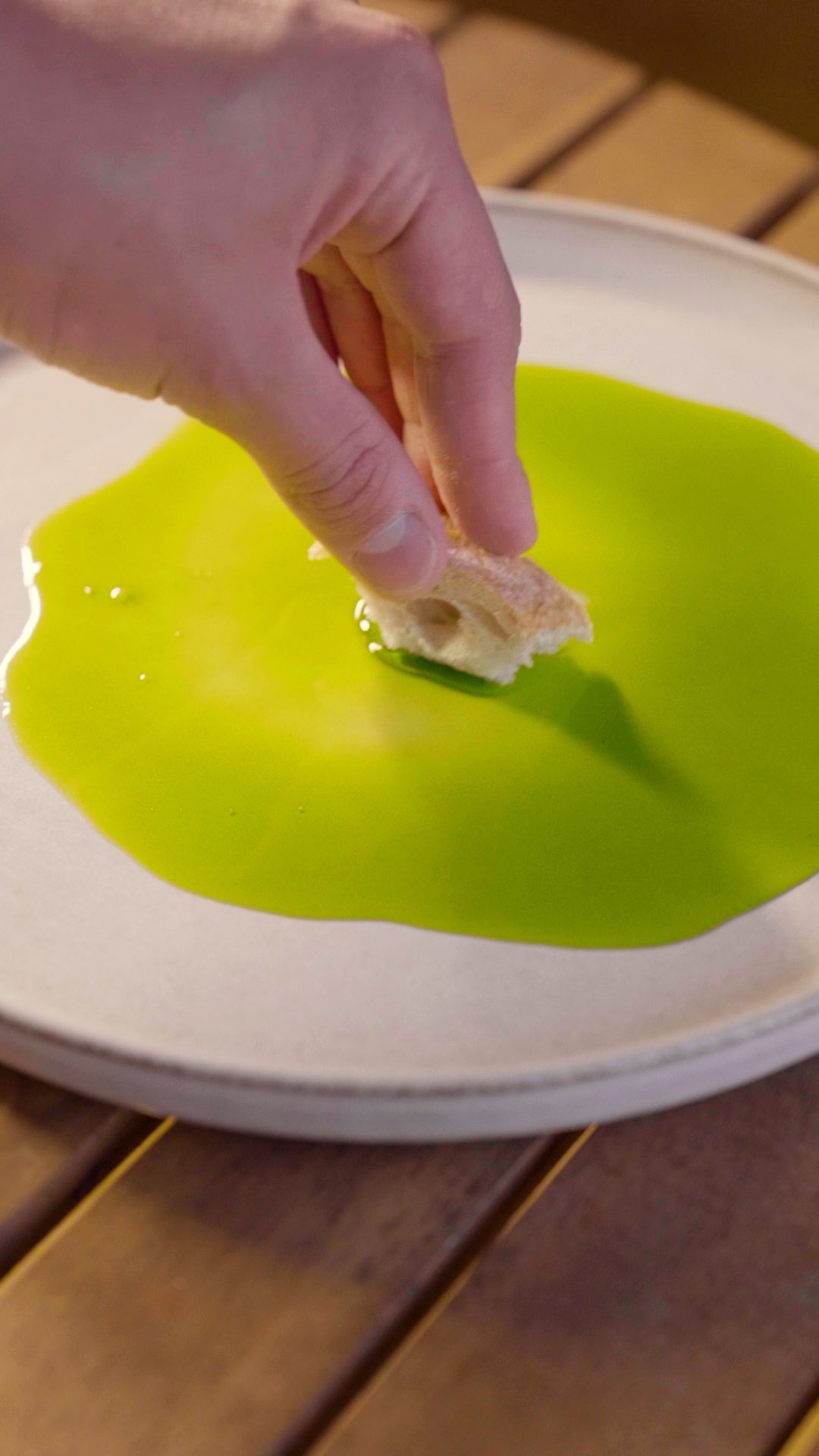 Hand dipping bread in bright green Oro Bailen Picual olive oil served on white plate