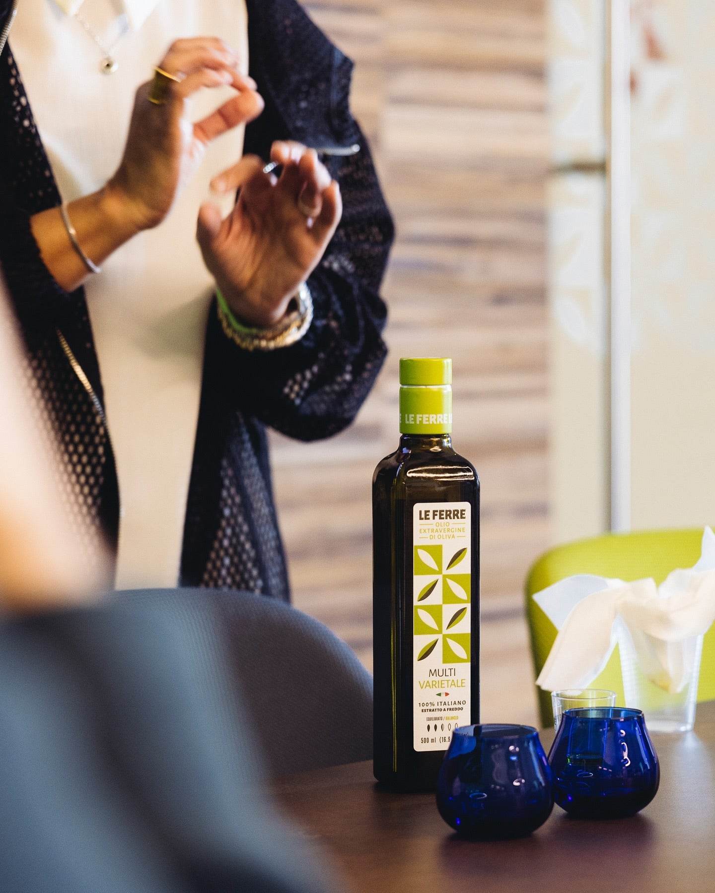 Best of Italiaanse Extra Vierge Olijfolie bottle displayed with blue glass cups on wooden table, lifestyle product photography