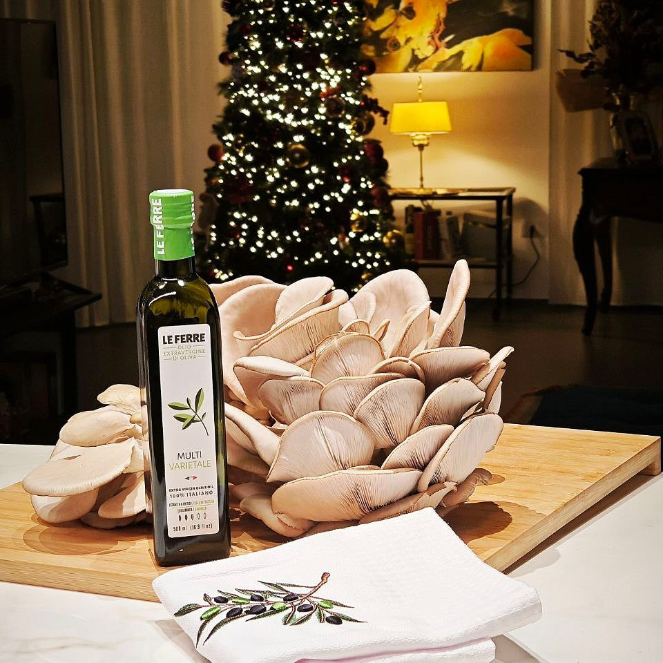 LeFerre Multivarietale olive oil bottle with oyster mushrooms on wooden board, Christmas tree in background