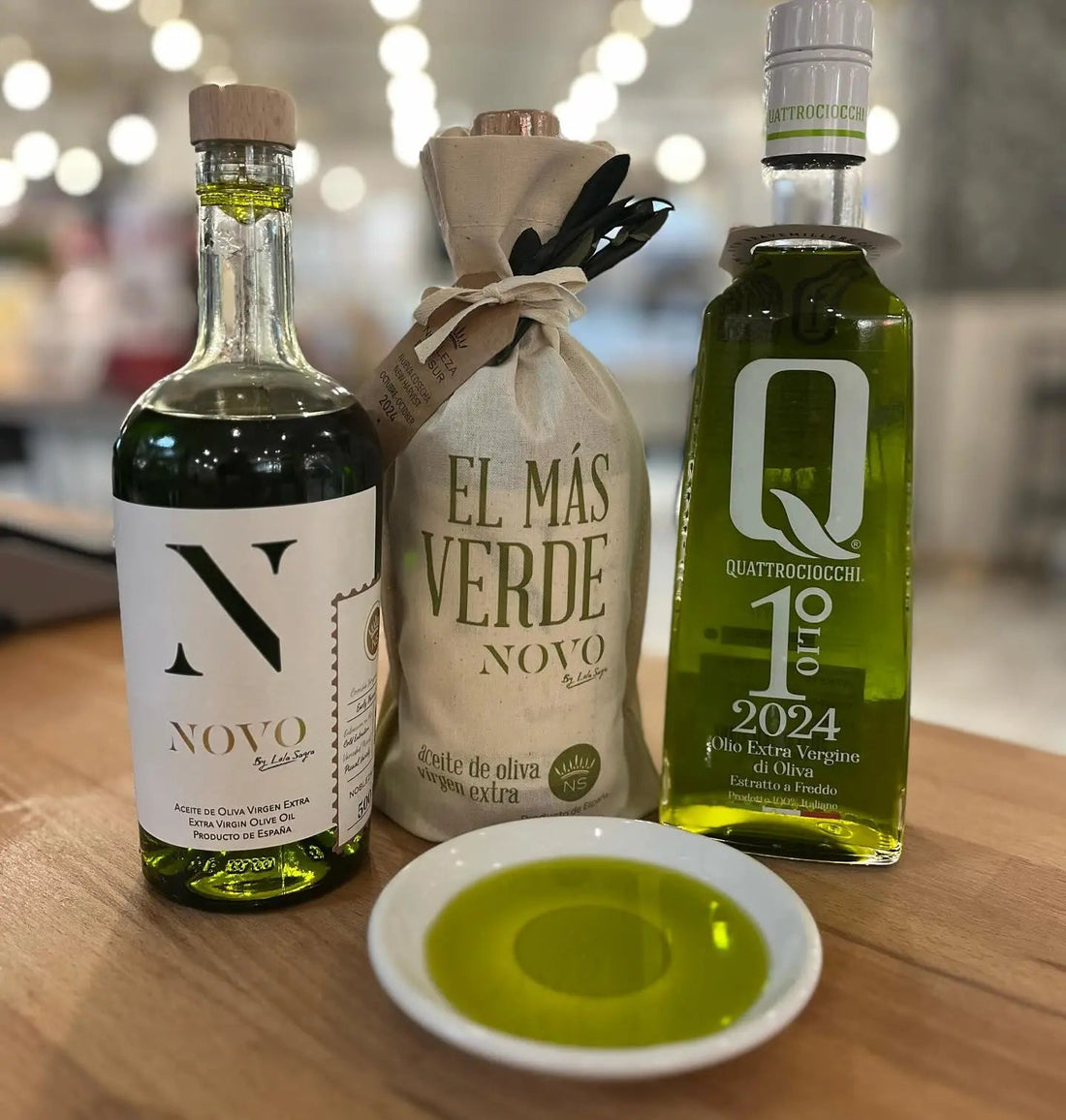 Helder groene olijfolie van de nieuwe oogst in een proefschaaltje naast twee flessen NOVO